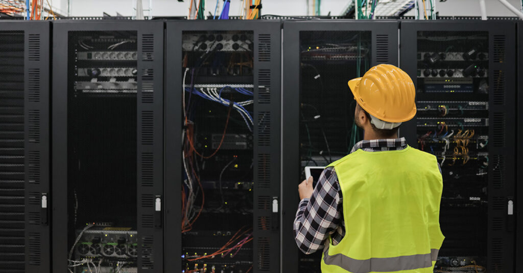 Young technician man working with tablet inside big data center room full of rack servers - Focus on man head