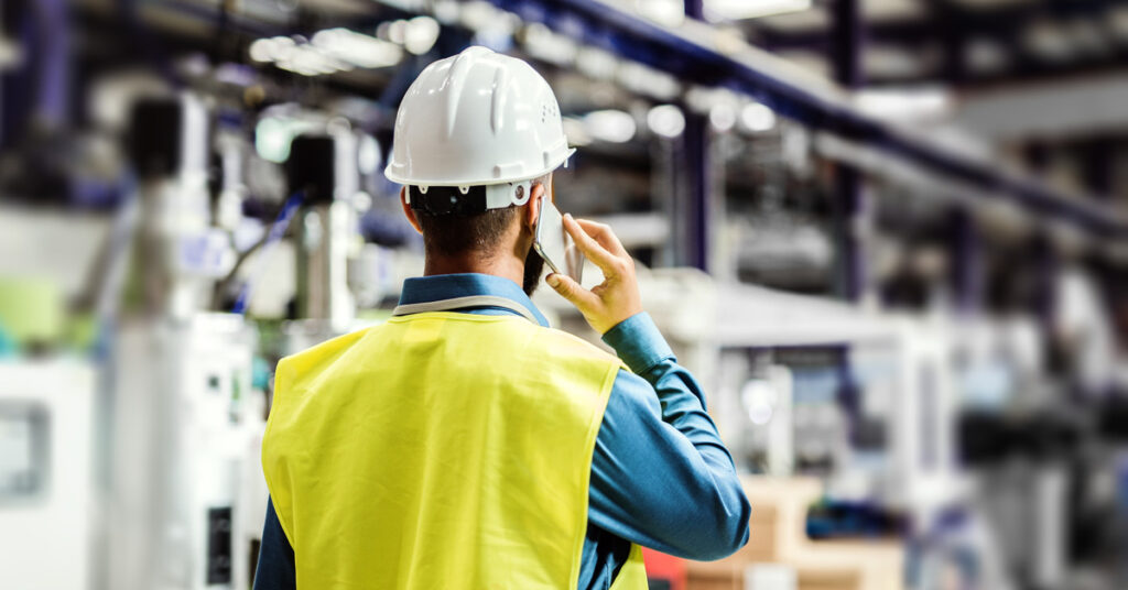 A rear view of a mature industrial man engineer with smartphone in a factory, making a phone call.